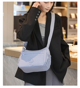 Close-up of light blue nylon crossbody bag featuring multi-zipper layers and adjustable strap