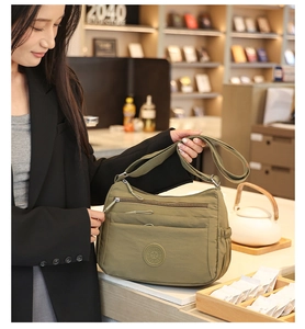 Olive nylon crossbody bag with multi-layer zippers and side pockets on a lifestyle setting