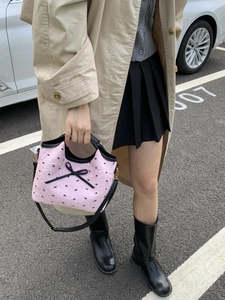 Sac à main plissé rose avec nœuds noirs présenté dans un cadre extérieur naturel