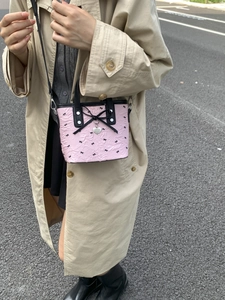Sac bandoulière rose à nœuds noirs et breloque cœur porté avec un trench classique