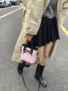 Mini sac à main rose avec nœuds noirs et breloque cœur sur un arrière-plan de rue urbaine