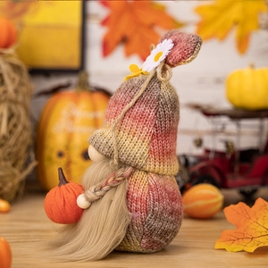 Detail of a knitted Thanksgiving gnome holding a small pumpkin with autumn maple leaves