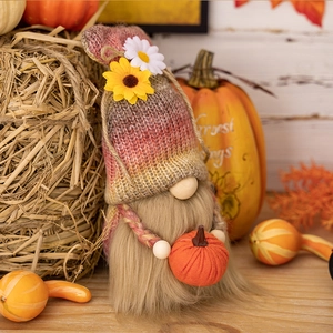 Detail of harvest gnome figurine holding an orange pumpkin with maple leaf background