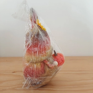 Detail of a knitted Thanksgiving gnome featuring a striped cap and holding a small pumpkin