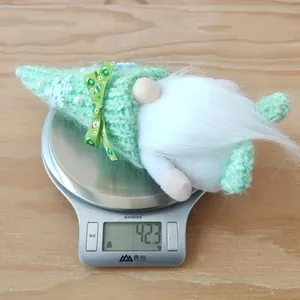 Green knitted Christmas gnome plush decoration with snowflake hat being weighed on a scale