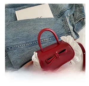 Détail d'un mini sac à main rouge avec nœud en cuir et dentelle blanche sur denim
