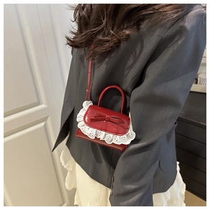 Donkerrode mini crossbody tas met kant en strik getoond op model in een huiselijke sfeer