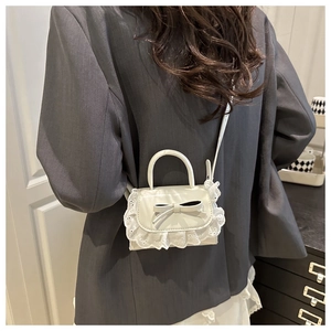 Détail d'un mini sac à main blanc avec dentelle et nœud porté à l'épaule par un mannequin