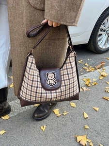 Brown checkered tote bag with teddy bear patch on an autumn street background