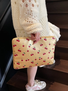Schicke goldene Laptoptasche mit Kirschmuster von Model in Alltagsszene gehalten