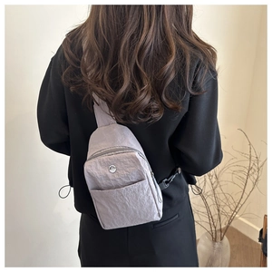 Detailansicht der Mini-Umhängetasche aus hellgrauem Knitterstoff mit M-Metalllogo