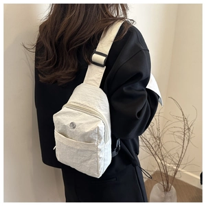 Rear view of off-white nylon chest bag with adjustable strap and buckle on model