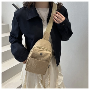 Detail of khaki nylon crossbody bag with zipper and logo patch worn by a fashion model