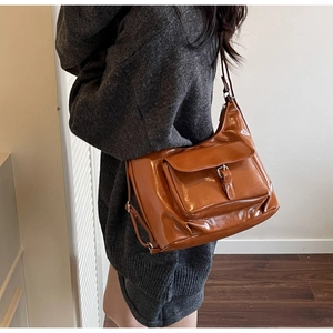 Gros plan d'un sac hobo brillant marron caramel avec boucle argentée porté à l'épaule