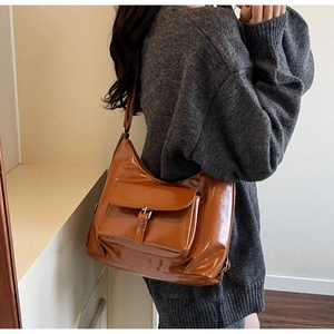 Detail of glossy brown tote bag with metal buckle pocket and high-shine patent texture