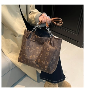 Detail of dark brown tote bag with vintage pattern and metal chain strap on trench coat