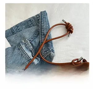 Macro detail of brown suede tote bag featuring slim leather strap with knot and silver hardware