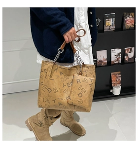 Detail of khaki tote bag with textured brand pattern and silver chain leather strap