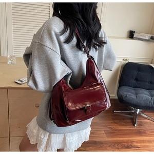 Détail d'un sac à bandoulière en cuir verni rouge foncé avec une poche avant utile