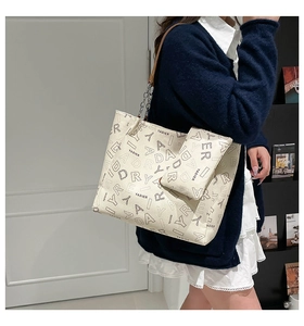 Model wearing a cream tote bag with letter print and metal chain leather strap