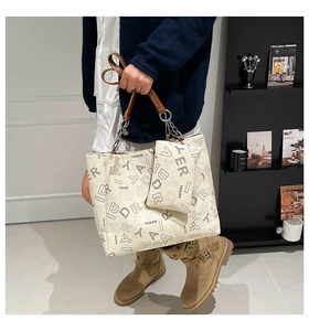 Detail of white tote bag with letter print and brown leather handles on a model