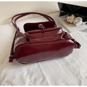 Détail d'un sac à main bordeaux brillant avec boucle argentée près d'un ordinateur