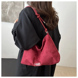 Detail of red suede tote bag featuring a knotted rope shoulder strap and modern logo patch