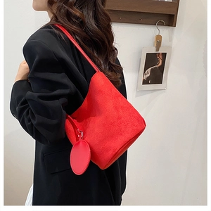 Modella che indossa borsa a secchiello in camoscio rosso con ciondolo su un blazer nero