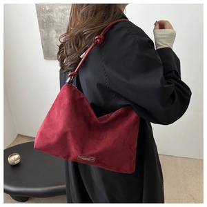 Detail of wine red suede shoulder bag with knot strap design and leather logo tag