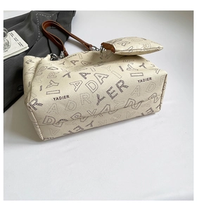 Detail of cream tote bag with YADIER letter print, leather straps, and small matching pouch