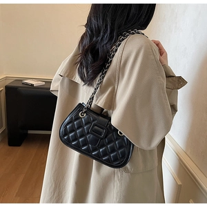 Dettaglio della borsa nera trapuntata con catena su modella con un trench
