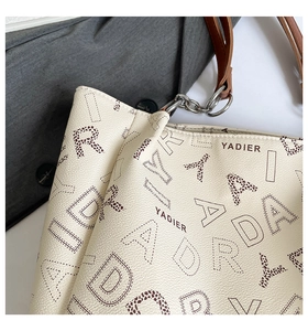 Close-up of off-white lychee pattern tote bag with vintage monogram and brown strap