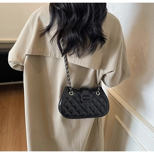 Detail of a black quilted crossbody bag with a gold chain strap and square buckle closure