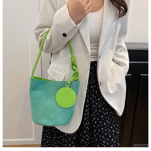 Dettaglio borsa a secchiello in camoscio teal con tracolla intrecciata verde neon e ciondolo