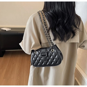 Close-up of black quilted leather shoulder bag with gold chain strap on model