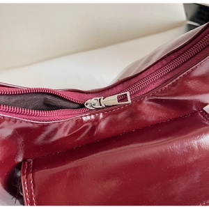 Détail d'un sac à main bordeaux brillant avec fermeture éclair argentée et coutures fines