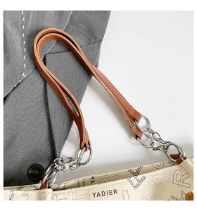 Detail of white tote bag with YADIER print, brown leather straps and silver chain link