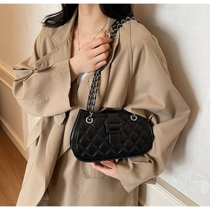 Detail of black quilted chain bag styled with a khaki trench coat for a modern look