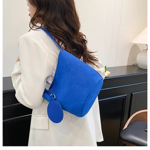 Dettaglio della borsa a secchiello in pelle scamosciata blu con ciondolo su blazer bianco