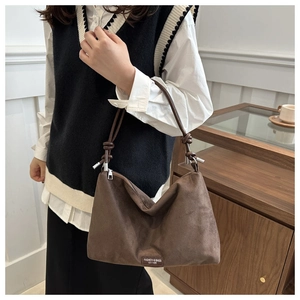 Detail of dark brown suede hobo bag featuring knotted shoulder strap and silver hardware