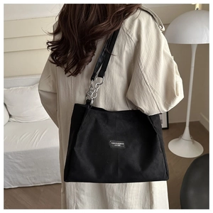 Dettaglio della borsa tote nera con patch logo in pelle e catena sulla modella