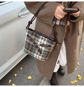 Détail d'un sac bandoulière en tweed vert avec sangle en cuir marron et boucles dorées