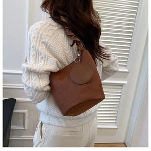 Dettaglio di una borsa a secchiello marrone scuro con tracolla intrecciata su modella