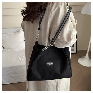 Dettaglio borsa a spalla scamosciata nera con tracolla a catena in pelle su cappotto beige