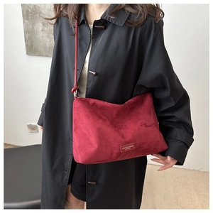 Detail of red suede crossbody bag with leather patch on a model in a black coat