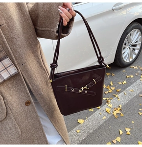 Détail du sac seau en cuir marron foncé avec bandoulière nouée dans un décor d'automne