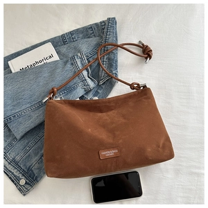 Detailed macro view of brown suede shoulder bag with leather logo tag on white fabric