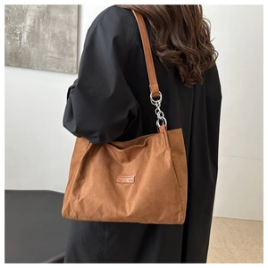 Dettaglio di una borsa tote in pelle scamosciata marrone con patch in pelle e fibbie argento