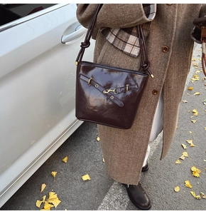Détail du sac seau en cuir marron foncé avec boucles dorées sur un manteau d'automne