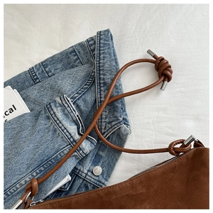 Close-up of brown suede crossbody bag with leather knot strap and silver hardware